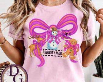 May include: Pink t-shirt featuring a whimsical design with a large purple bow and postage stamp-style illustrations of a snowman, reindeer, and gingerbread man. The words "PRIORITY MAIL" are printed on the shirt.