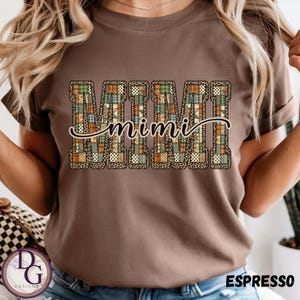 Peut inclure: T-shirt couleur expresso avec le mot "MIMI" dans un motif patchwork avec des motifs léopard et écossais. Le mot "mimi" est écrit en cursive sur les lettres patchwork. Le t-shirt est un col rond.