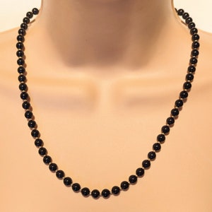 May include: A black onyx beaded necklace with gold accents. The necklace is made of round beads and is approximately 18 inches long.
