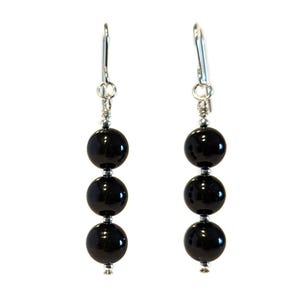 May include: A pair of silver dangle earrings with three black onyx beads on each earring.