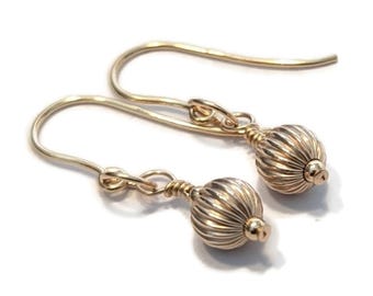 May include: A pair of gold-colored drop earrings. Each earring features a ribbed, spherical bead suspended from a curved ear wire. The beads have a small, rounded cap at the top and bottom. The earrings are displayed against a white background.