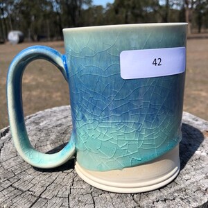 May include: A blue and green ceramic mug with a crackled glaze. The mug has a white handle and a white base. The mug is labelled with the number "42".