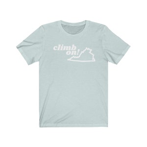 Può includere: Una t-shirt blu chiaro con un contorno bianco dello stato della Virginia e il testo "climb on!" in bianco.