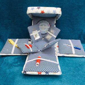 May include: A white and blue striped fabric sewing box with a star pattern on the top and bottom. The box is open and filled with sewing supplies, including needles, thread, and a pincushion.