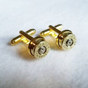 Peut inclure: Une paire de boutons de manchette dorés représentant une douille de balle de calibre 9 mm Luger avec les mots "Blazer" et "9 mm Luger" gravés sur le côté.