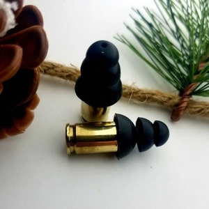May include: Two black silicone earplugs attached to gold-colored bullet casings. The earplugs are designed to reduce noise.