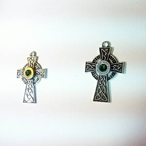 May include: Two silver Celtic cross pendants with green gem accents. The larger pendant has the words "God & Guns" inscribed around the gem.