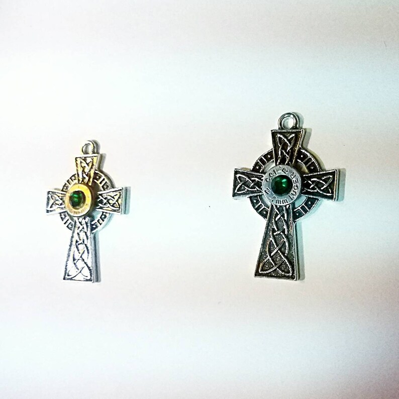 May include: Two silver Celtic cross pendants with green gem accents. The larger pendant has the words "God & Guns" inscribed around the gem.