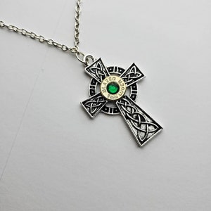 May include: A silver Celtic cross pendant necklace with a green gem in the center of a gold bullet casing. The bullet casing is engraved with "9mm BLAZER LUGER".