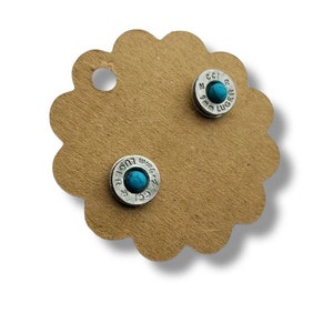 May include: A pair of silver bullet earrings with turquoise stones. The earrings are on a brown card with a scalloped edge.