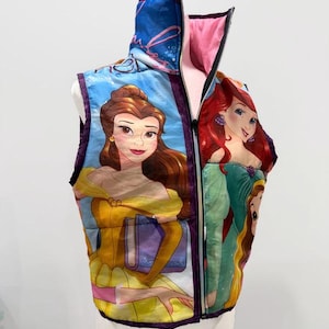 Könnte beinhalten: Eine farbenfrohe Weste mit Illustrationen der Disney-Prinzessinnen Belle und Arielle. Die Weste hat eine blaue Außenseite, ein rosa Innenfutter und einen durchgehenden Reißverschluss. Belle trägt Gelb und Arielle Grün, beide in ihren ikonischen Outfits.
