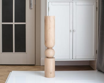 Puede incluir: Un jarrón alto de madera con un diseño redondeado y bulboso en el medio. El jarrón está hecho de madera de color claro y tiene un aspecto natural y sin terminar.