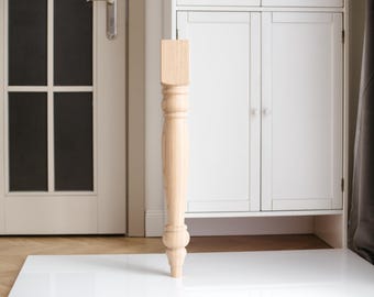 Puede incluir: Una pata de mesa de madera con un diseño torneado. La pata es de color marrón claro y tiene un acabado liso.