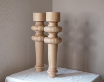 May include: Two wooden table legs with a turned design. The legs are light brown and have a smooth finish.