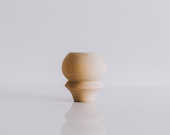 May include: A light brown wooden vase with a rounded top and a flared base.