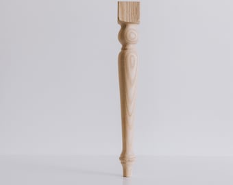 May include: A wooden table leg with a turned design and a square top. The leg is light brown in color and has a smooth finish.