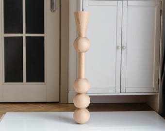 May include: A tall, wooden sculpture with a rounded, vase-like top and three spherical sections. The sculpture is light brown in colour and has a smooth, polished finish.