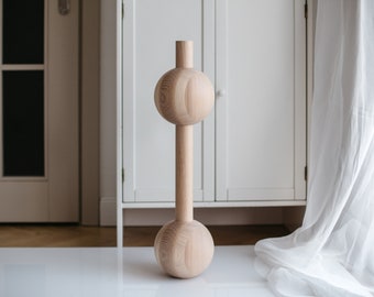 Puede incluir: Un jarrón de madera con un cuerpo cilíndrico y dos bulbos redondos y esféricos en la parte superior e inferior. El jarrón es de color marrón claro y tiene una veta de madera natural.