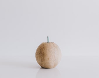 May include: A wooden sphere with a small metal rod protruding from the top. The sphere is light brown and has a smooth, polished finish.