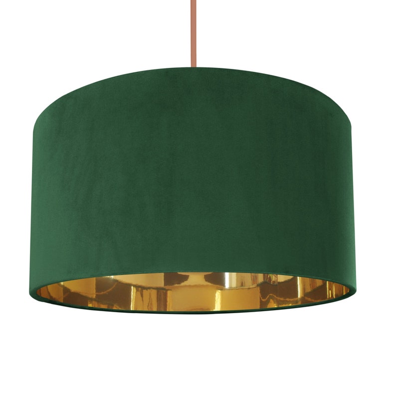 Op de afbeelding: Een groene fluwelen lampenkap met een gouden metallic voering. De lampenkap is cilindrisch en heeft een gladde, zachte textuur.