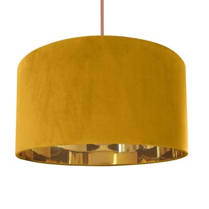 May include: A mustard yellow velvet lampshade with a gold metallic trim. The lampshade is cylindrical in shape and has a smooth, soft texture.
