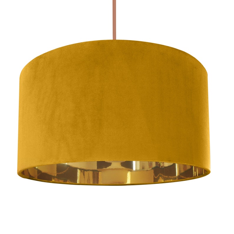 May include: A mustard yellow velvet lampshade with a gold metallic trim. The lampshade is cylindrical in shape and has a smooth, soft texture.