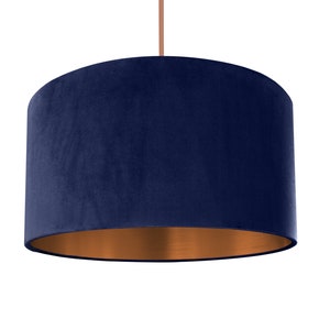 May include: A navy blue velvet lampshade with a copper bottom. The lampshade is cylindrical and has a smooth, soft texture.