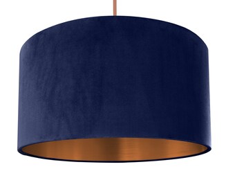 Op de afbeelding: Een donkerblauwe fluwelen lampenkap met een koperen onderkant. De lampenkap is cilindrisch en heeft een gladde, zachte textuur.