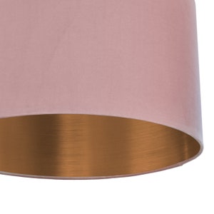 May include: A close-up of a pink lampshade with a metallic bronze interior. The lampshade has a cylindrical shape and a soft, velvety texture. The bronze interior reflects light, creating a warm glow.