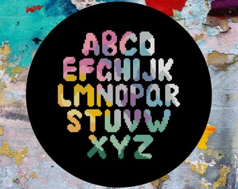 May include: A black circle with a white background and a colorful alphabet in a pixelated style. The letters are in different colors, including pink, blue, yellow, green, and purple.