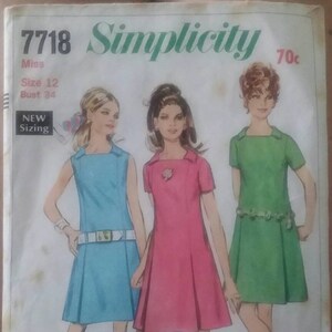 May include: A vintage Simplicity sewing pattern for a dress, pattern number 7718, size 12, bust 34. The pattern shows three women wearing different coloured dresses, one in blue, one in pink, and one in green. The pattern is labelled "New Sizing" and costs 70 pence.