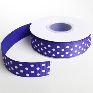 Può includere: Un rotolo di nastro viola con pois bianchi. Il nastro è su un rotolo bianco.