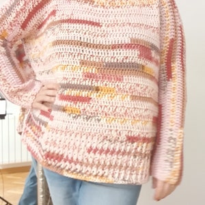Puede incluir: Un suéter de punto de crochet a rayas rosa, marrón y naranja con cuello alto.
