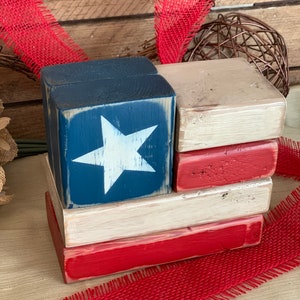 May include: A wooden block sculpture of the American flag. The blocks are painted red, white and blue. The top block features a white star on a blue background.