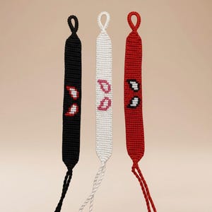 May include: Three handmade friendship bracelets in black, white, and red. Each bracelet features a unique design with embroidered accents. The black and red bracelets have white and red accents, while the white bracelet has pink accents.