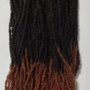 May include: Two bundles of synthetic dreadlocks with a black to brown ombre color. The dreadlocks are made of a soft, textured material.