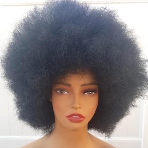 May include: A mannequin head with a large, voluminous black afro wig. The mannequin has brown eyes, full red lips, and a neutral skin tone. The wig is styled in a round, full shape.
