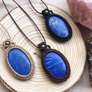 Peut inclure: Trois colliers avec des pierres de lapis-lazuli enveloppées de cordon macramé. Les pierres sont d'un bleu profond avec des reflets dorés. Les cordons sont marron, noir et beige.