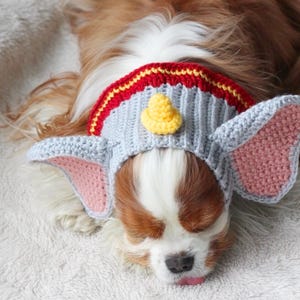 A beginner-friendly crochet pattern for a Flying Elephant dog snood. This dog snood features a grey and pink colourway. The Flying Elephant dog snood is modeled by a Blenheim Cavalier King Charles Spaniel.