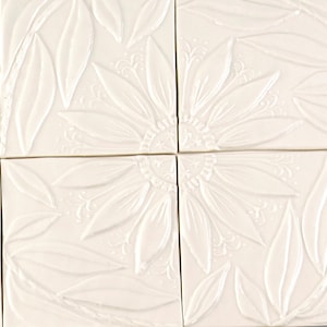 May include: Four white ceramic tiles featuring an embossed design of a sunflower and leaves. The tiles are arranged in a square formation.