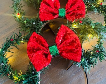 May include: Three pairs of red and green sequined bow headbands with a green garland headband. The garland has small white and green lights.