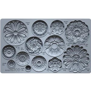 May include: A gray silicone mold featuring various rosette designs in different sizes. The mold includes floral and circular patterns, with measurements in milliliters and grams. The text "ROSETTES IOD" is printed on the mold.