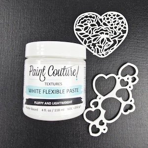 May include: A jar of "Paint Couture" white flexible paste, 4 fl. oz. / 118 ml, sits next to two white heart-shaped decorative cutouts. One heart has a floral design, and the other has multiple hearts.