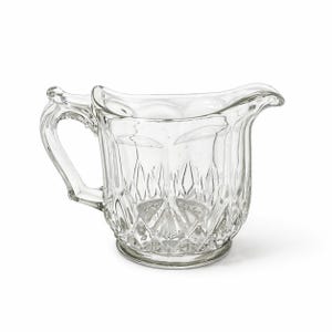 May include: Clear glass creamer with a handle and a spout. The creamer has a diamond pattern on the body and a rounded base. The handle is curved and attached to the side of the creamer. The spout is slightly flared.