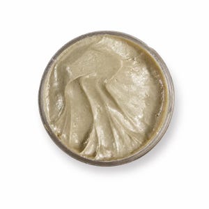 May include: A circular container filled with a thick, smooth, light olive-green paste. The surface of the substance shows distinct, curved ridges and swirls created by a tool, with a glossy sheen reflecting light across the textured cream.