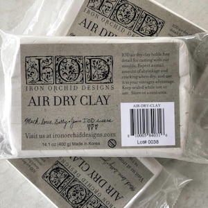 May include: White air dry clay packaged in clear plastic. The label reads "Iron Orchid Designs Air Dry Clay" with the text "14.1 oz (400 g) Made in Korea". The package also includes the text "Air-Dry-Clay".