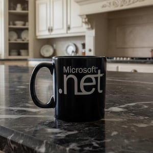 May include: A black ceramic mug with the Microsoft .net logo in white. The mug has a curved handle and is sitting on a dark, marbled countertop in a kitchen setting.
