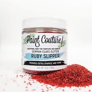 May include: A jar of "Paint Couture" German glass glitter in "Ruby Slipper" color. The jar is filled with red glitter and has a white lid. The label reads "Exceptional Paint for Furniture and Cabinets" and "Provides Extra Sparkle and Shine". Net weight is 5oz.