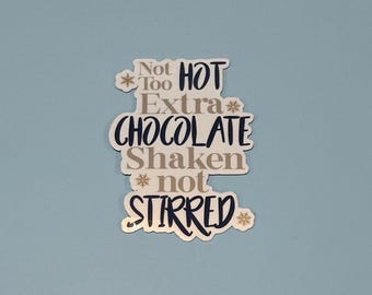 May include: A sticker with the words "Not Too Hot Extra Chocolate Shaken not Stirred" in a mix of navy blue, gray, and white. The sticker has a light blue background and snowflake accents.