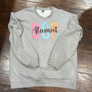 May include: Gray sweatshirt with a colorful "DCP Alumni" design and a small Mickey Mouse icon.